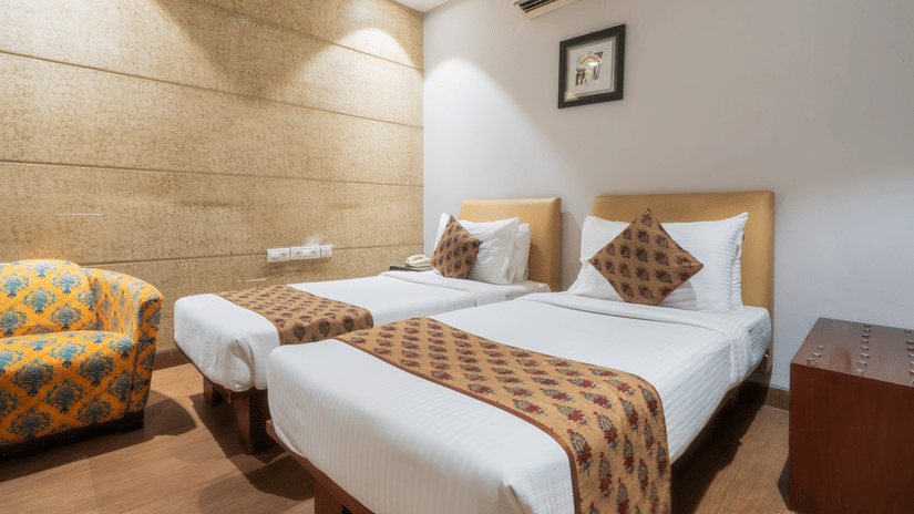 A room at Cosy Grand at Chanakyapuri By The Cosy Hotels featuring two similar looking beds, a bedside table, and a sofa chair.