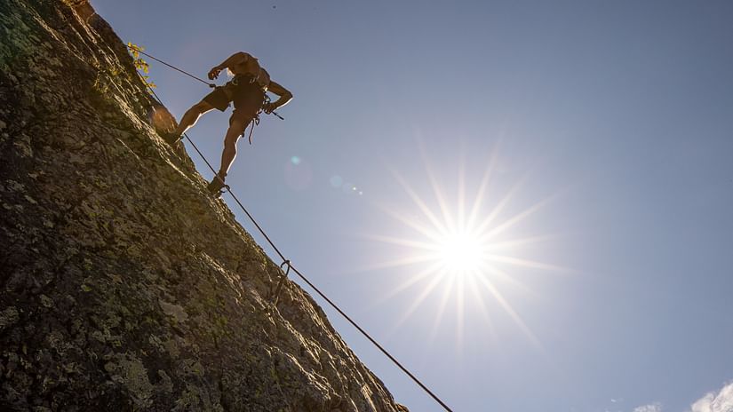 Silhouette of a rock climber scaling a cliff at sunset or sunrise, with the sunburst creating a dramatic backdrop against the sky