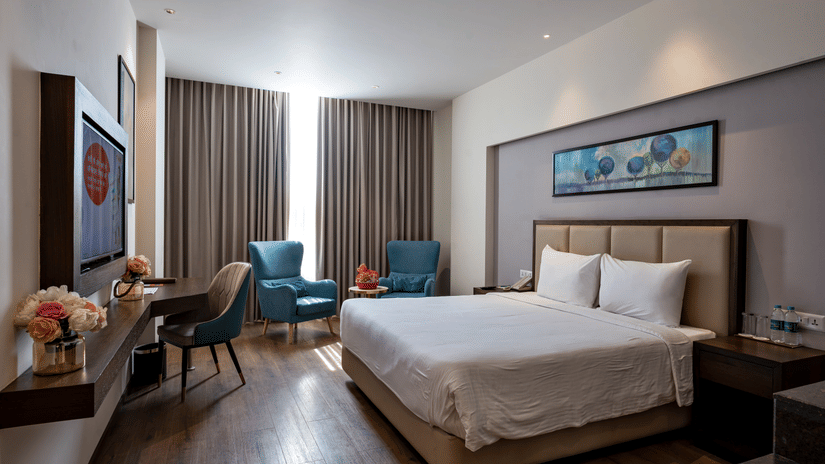 A bedroom at Geeta Sarovar Portico, Panipat featuring a double size bed, a flat TV screen on the wall, a chair, and a seating area.