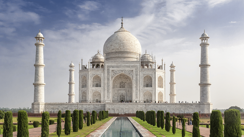 A facade view of Taj Mahal in all its glory, with a waterbody in the centre and small shrubs next to it. Agra is one of the best places to visit for a road trip from Delhi.