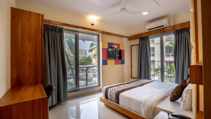 Home2 Suites & Service Apartments featuring a bed facing the TV on the wall with the door to balcony next to it, ready to be booked with exciting offers at Home2 India available on the official website
