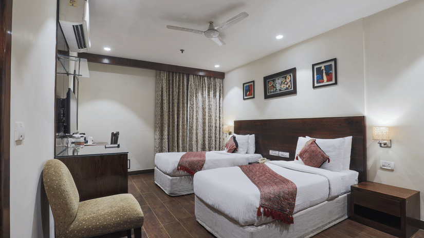 Twin room with wood flooring, red accent throws, and framed wall art at Hotel Bluestone (Nehru Place) by The Cosy Hotels