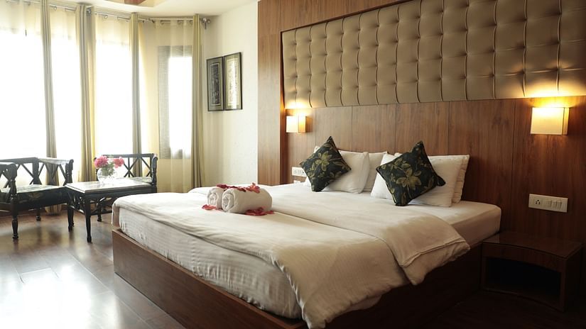 Well-lit room at Hotel Mount View with a plush double bed, elegant headboard, cosy seating area by large windows, and warm wooden accents.