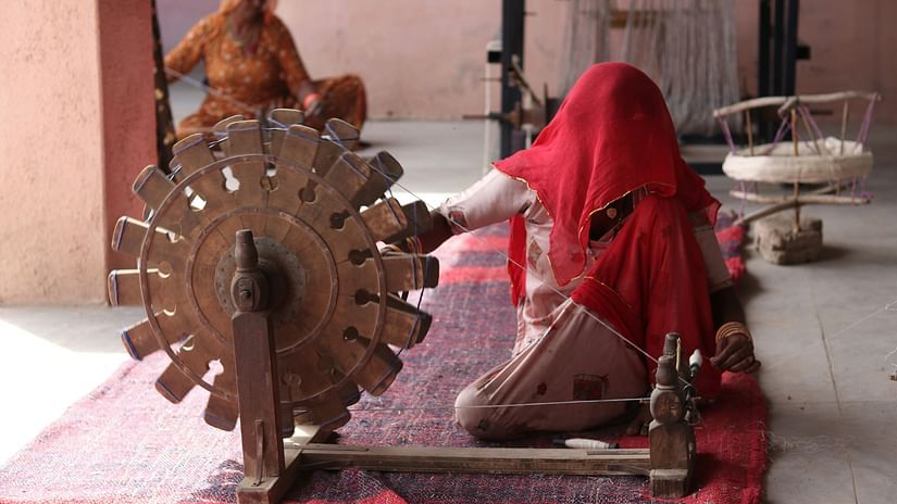 A woman with a cloth over her head spinning a chakra with a red cloth on the floor
