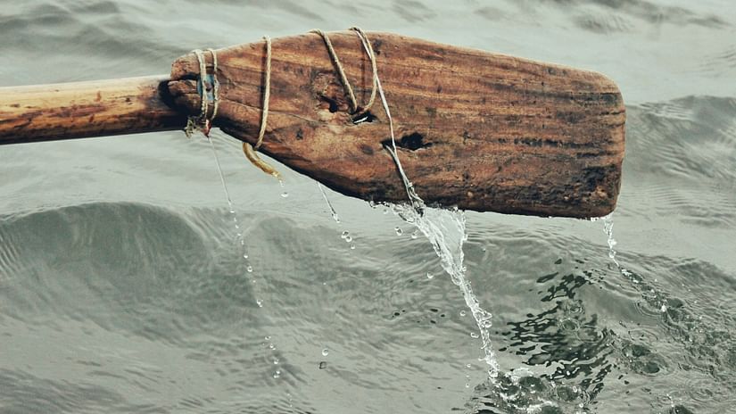 A close up shot of a beat up oar of a boat with a waterbody in the background
