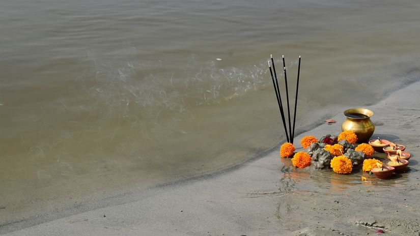 A picture of lit incense sticks, flowers and a copper bowl next to a river