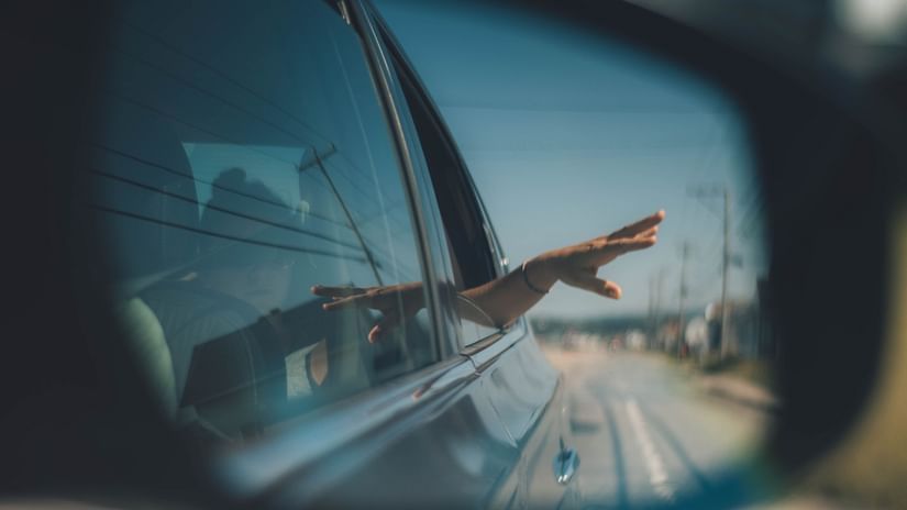 A view from the side mirror of a passenger putting their hand out of the window of a car 