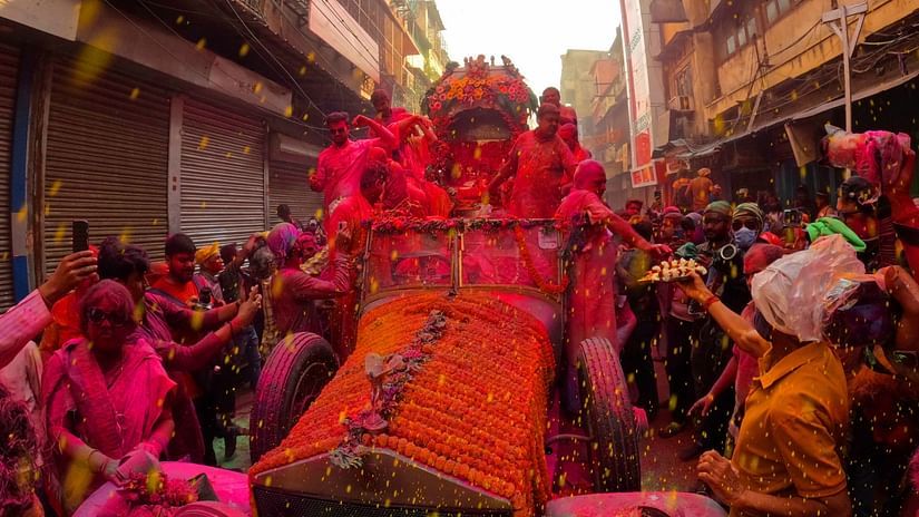 a procession with a statue on the road with holi colours put on the idol and people next to it
