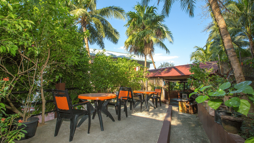Outdoor seating with coconut trees among other trees at Love Garden in Hotel Shompen, one of the best hotels in Port Blair.