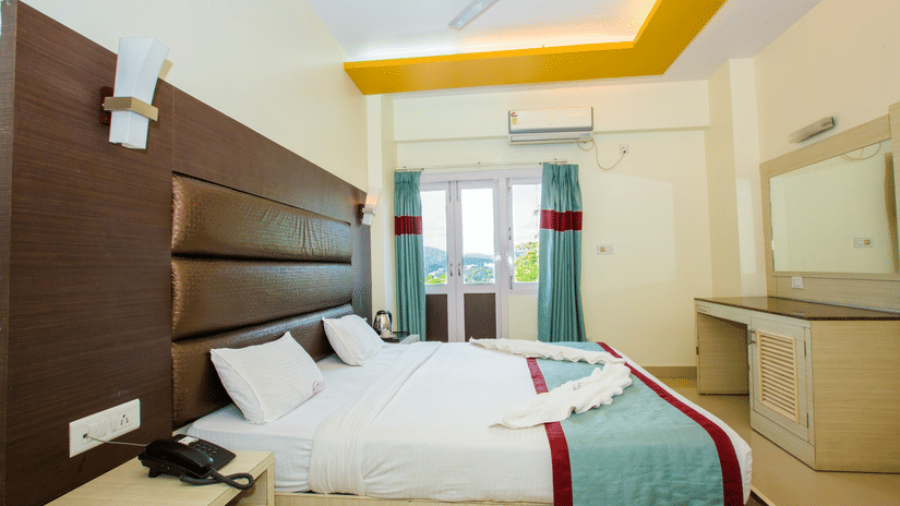 Interiors of Sea View Room, one of finest Port Blair Stay at Hotel Shompen, featuring a large bed, upholstered headboard, dressing table, and a large window offering outdoor views.