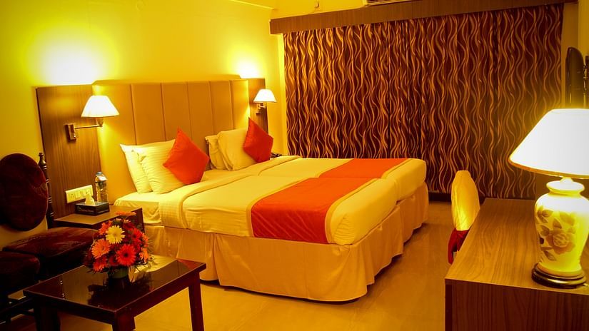 Hotel Yasodha Towers - Interior view of a bedroom containing a queen size bed illuminated with yellow coloured lamps 