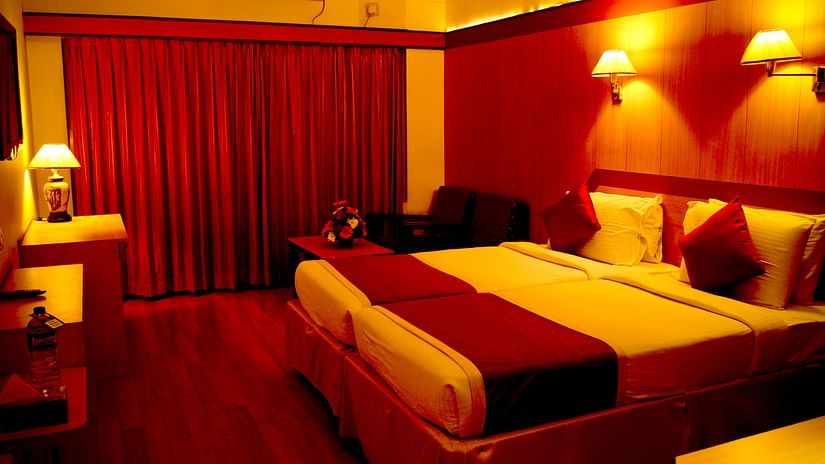  Hotel Yasodha Towers - Interior view of a bedroom featuring a double bed, wooden flooring and red curtains in yellow ambient lighting