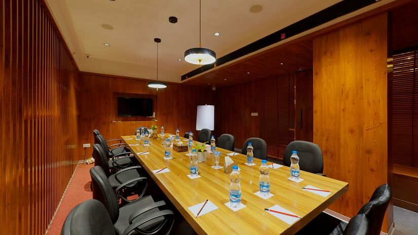A modern and well-equipped meeting room at Icon Boutique Hotel by Bhagini, Domlur, with a long conference table, chairs, and a wooden wall.