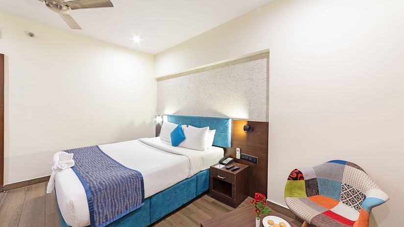 A spacious and well-lit hotel room at Icon Boutique Hotel by Bhagini, Domlur, with a comfortable bed, a seating area, and a colorful sofa.