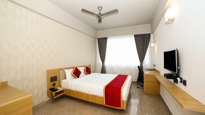 A double bed, a wall-mounted television, and a wooden desk at Icon Express By Bhagini, Mahadevapura.