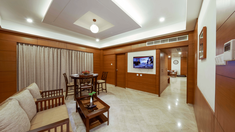 A suite at JP Hotel Chennai featuring living area with wooden furnishings, and sofas with a coffee table facing the TV on the wall.