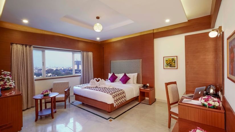Elegant room with a king bed, table and chair with natural lighting at JP Hotel Chennai.