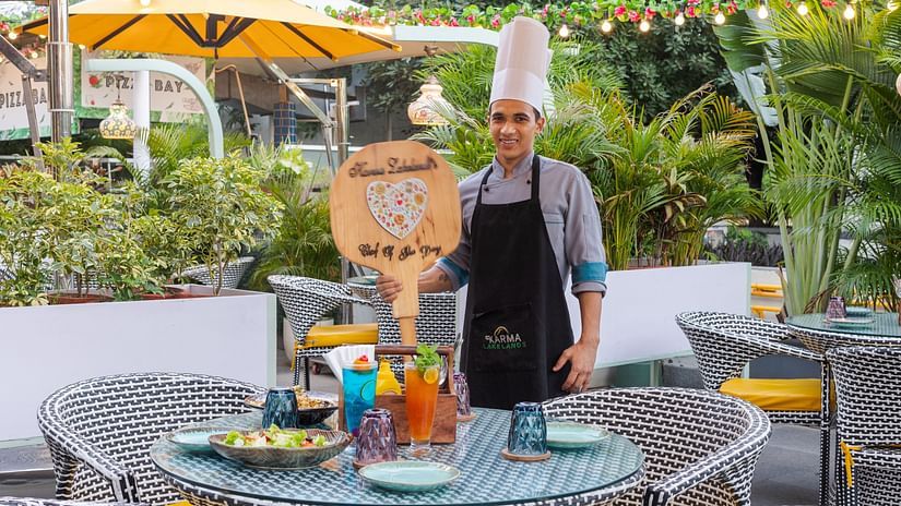 A chef holding a signage next to a table at Pizza Bay - Karma Lakelands