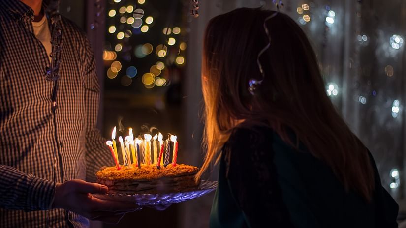 a person holding a cake while another is blowing out the candles on it - Karma Lakelands.