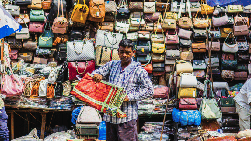 A shopkeeper folding a bag with numerous other purses for women kept neatly on the wall