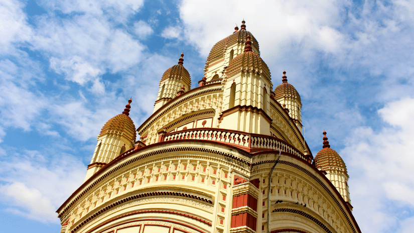 A view from below of the Dakshineswar Kali Mata Mandir with white clouds on a blue sky in the background.