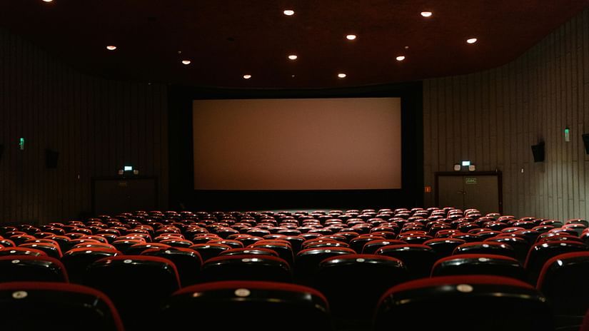 An empty theatre with rows of red seats facing a large movie screen.