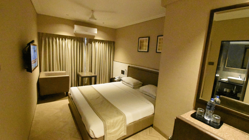 A bedroom featuring a bed, a sofa facing a coffee table, a wall-mounted TV, and a vanity in the foreground |  Kings International Juhu