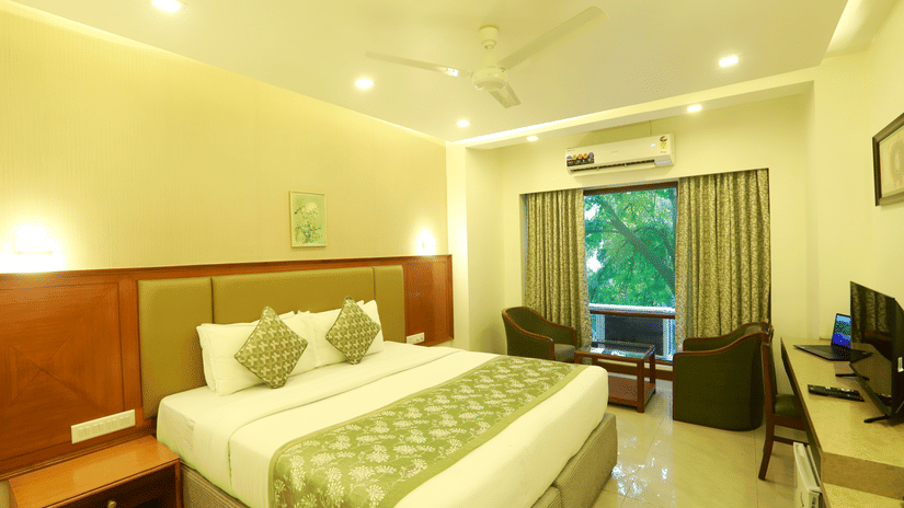 The Deluxe Room at Kohinoor Executive featuring a double bed, seating area, and warm lighting.