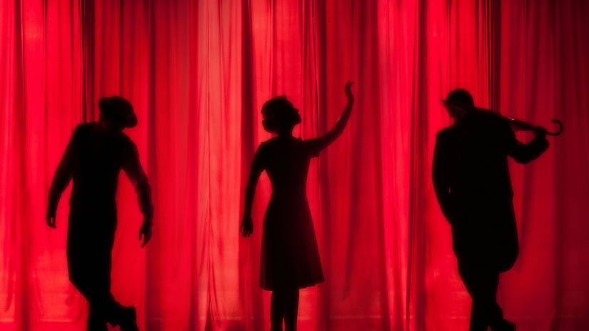 three people on the stage performing in a theatre with red curtains in the background