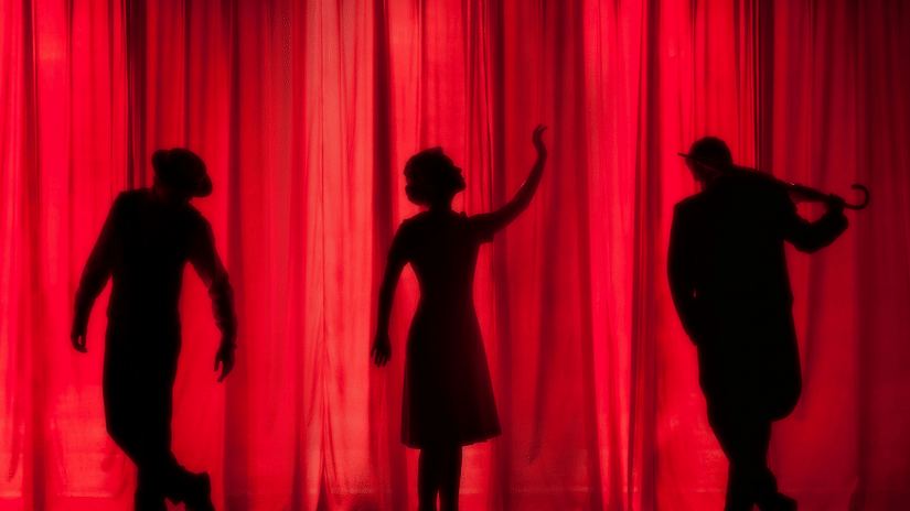 Three people on the stage performing in a theatre with red curtains in the background at Qatar National Convention Centre.
