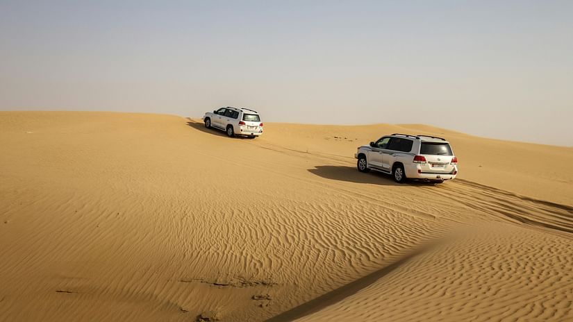 Two SUVs driving through the dunes in a desert on a clear day