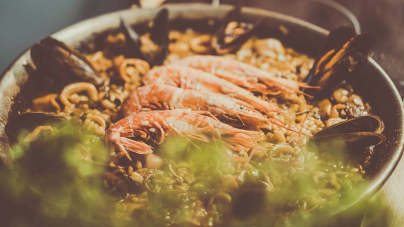 A close-up of a pot of seafood stew with prawns, mussels, and crabs. The dish has a green, foamy sauce.