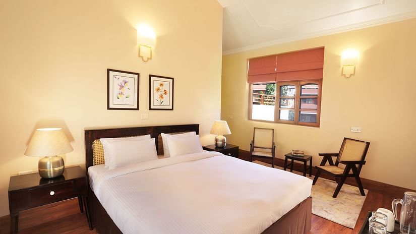 An image of a deluxe room with a double size bed, bedside table with lamps on either side, a chair, and other decorative items - Lamrin Boutique Cottages, Rishikesh
