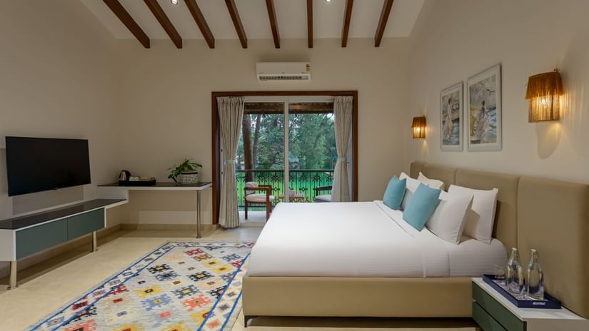 A bright, spacious bedroom with a large bed, wooden ceiling beams, and a view of a lush outdoor area through open doors - Lamrin Morjim Goa