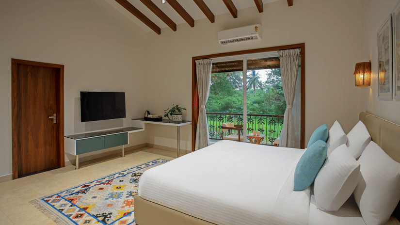 Spacious room with a plush bed, wall-mounted TV, and a balcony sitting area – Lamrin Morjim Goa