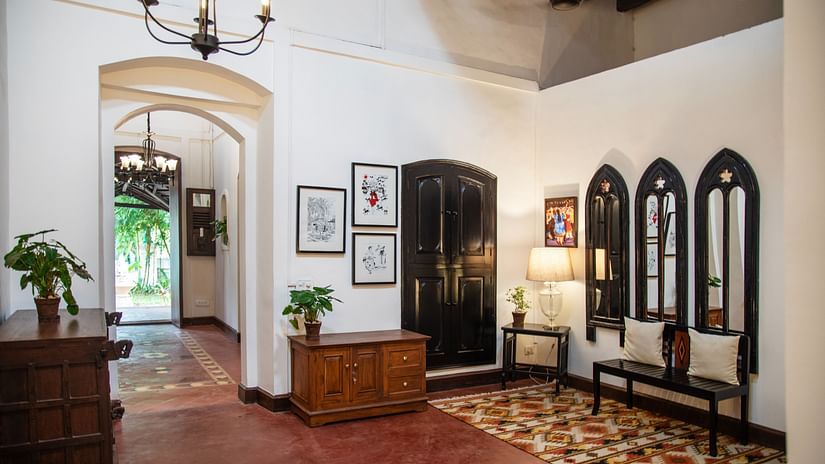 An image of a huge lobby where various decorative items are placed on top of the cabinets and shelves, there is another table with lamp and three vintage style window near it - Lamrin Ucassaim Hotel, Goa