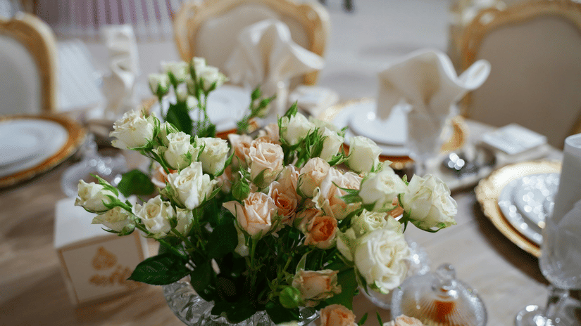 A close up shot of a beautiful flower vase with a lot of white and pink roses on a dining table.