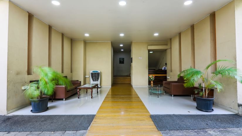A lobby at Magnus Vosiv Suites, Kalyani Nagar showcasing seating areas on either side with sofa sets. The space also has some flowered pots.