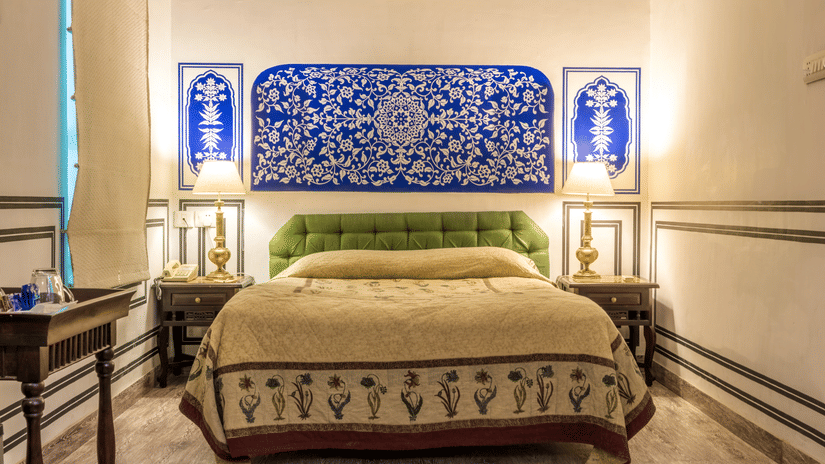 Deluxe Room at Mandawa Haveli, Jaipur featuring a king size bed, bedside table with lamps on either side, and a table with tea and coffee maker.