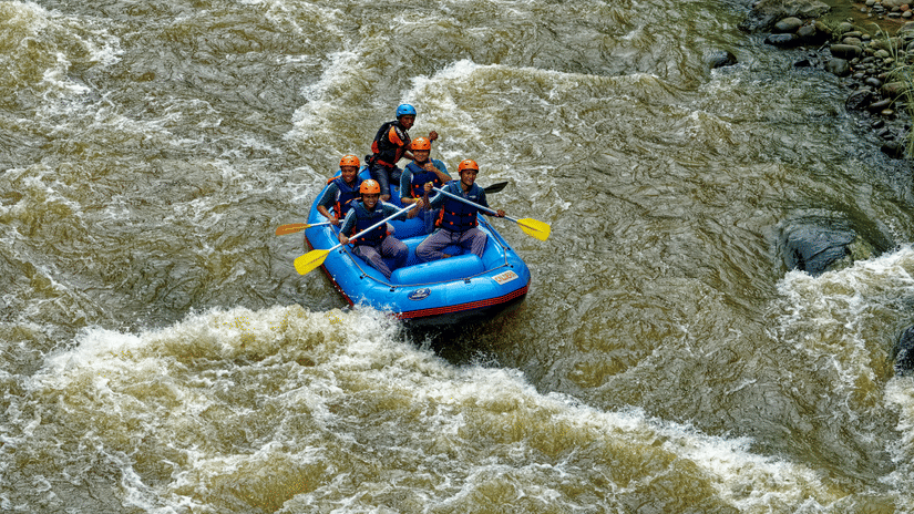 5 people wearing protective gear seen rafting across a water stream with a strong current.