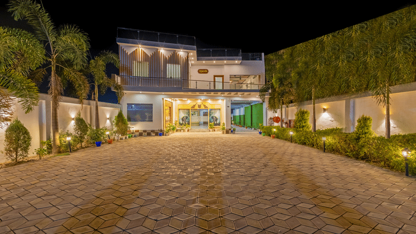 A wide-angle night view of a paved resort entrance with palm trees and warm lighting under a dark sky - Nature Trails Rishikesh