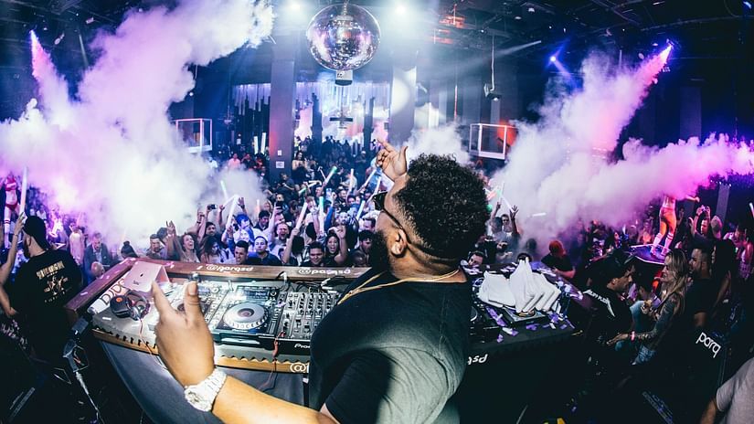 A dj playing songs with a large crowd dancing to the beats and pink smoke on either side
