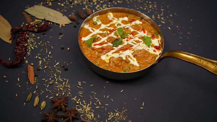 A curry placed in a bowl garnished with mint placed on a tale with spices around.