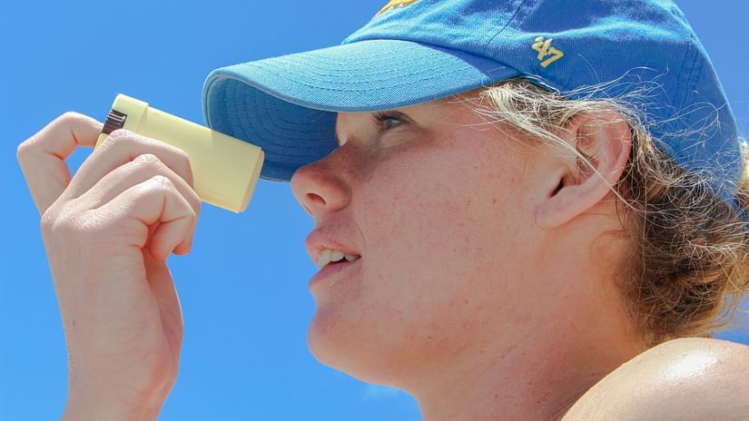 A close up shot of a woman wearing a hat using a sunscreen on her face.
