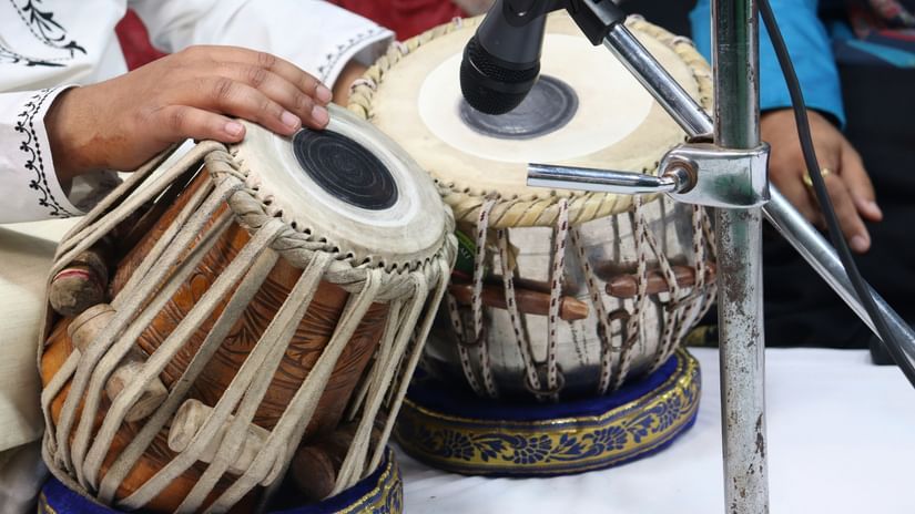 Close view of hands playing a pair of tabla drums with mikes nearby.