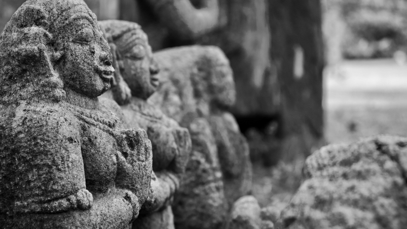 Ancient stone carvings depicting elephants, weathered by time, arranged along a historic monument site amid natural surroundings and foliage