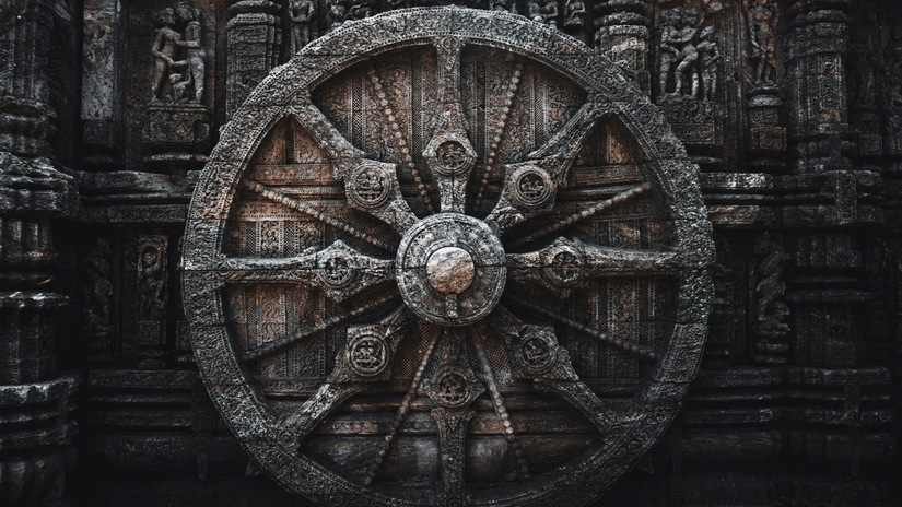 Ornate stone wheel carved into the Sun Temple facade, illuminated against dark stone, revealing intricate spokes, floral patterns, and timeless craftsmanship.