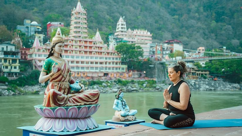elderly woman meditating in front of a statue of Parvati on the Ganges