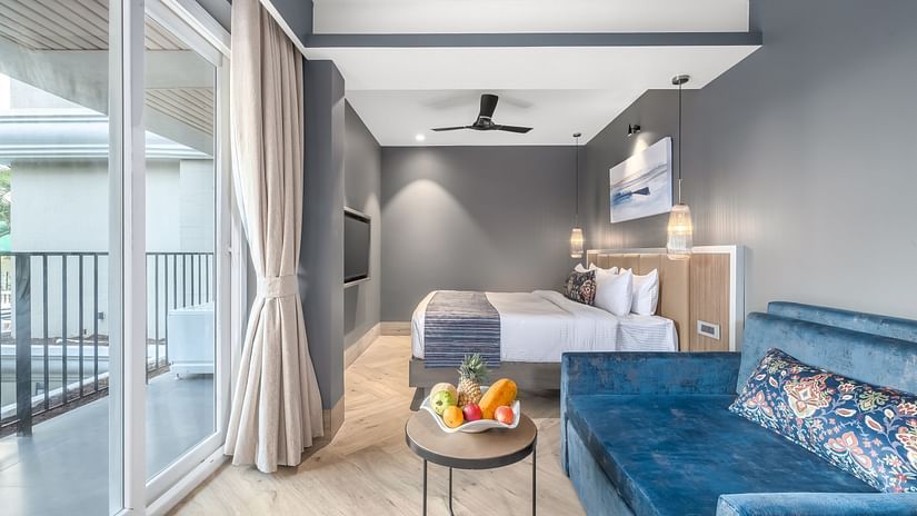 Pool View Room with modern grey interiors, a plush blue sofa, large bed, balcony access, and a fruit bowl on the coffee table at Ocean Palms Goa