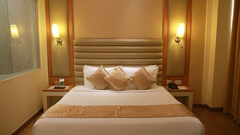 A warm-lit room featuring a double bed with pillows and cushions arranged and a couple of nightstand on both sides